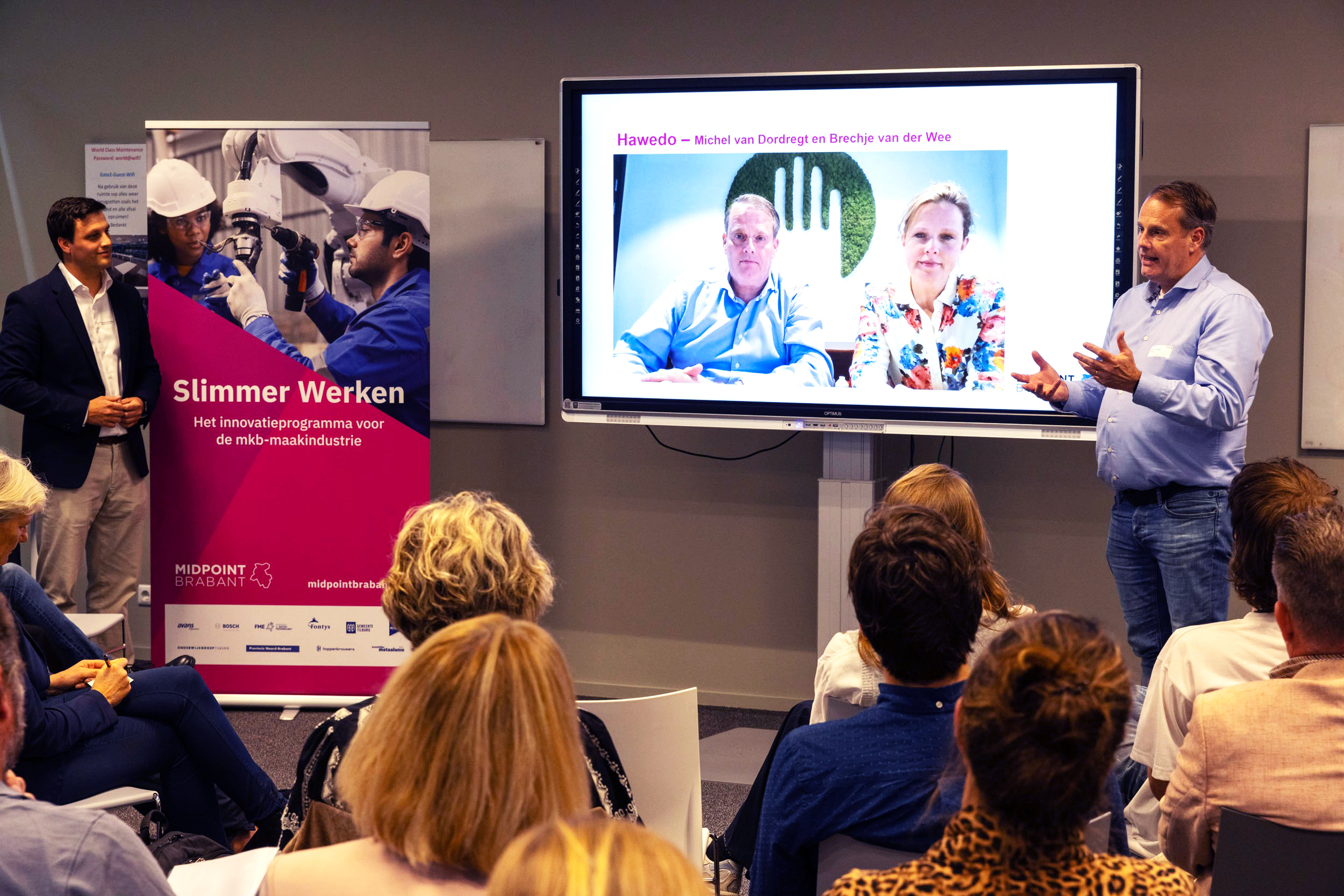 Gedurende de kick-off van het Lerend Netwerk Pilot Duurzaam Produceren geeft een meneer een presentatie op een scherm. Het publiek luistert.