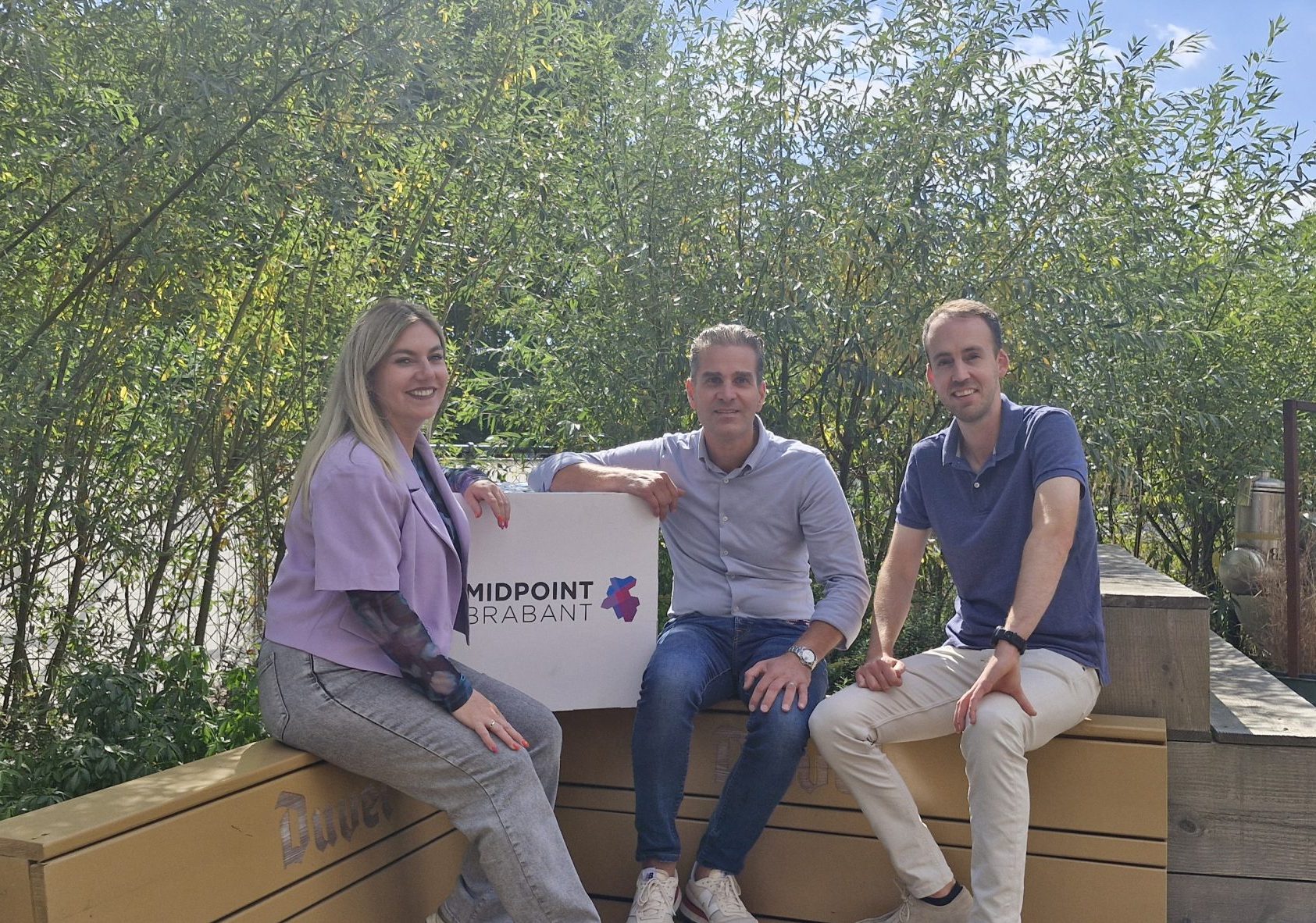 Remco Coppejans (Partnermanager bij Midpoint Brabant), Jesle Tuerlings (HR- en payrolladviseur Mettom Payrolling), Jeroen Jacobs (algemeen directeur Mettom Payrolling) poseren tijdens het partnerschapmoment. Ze zitten op een bankje naast de kubus met het Midpoint Brabant logo erop.